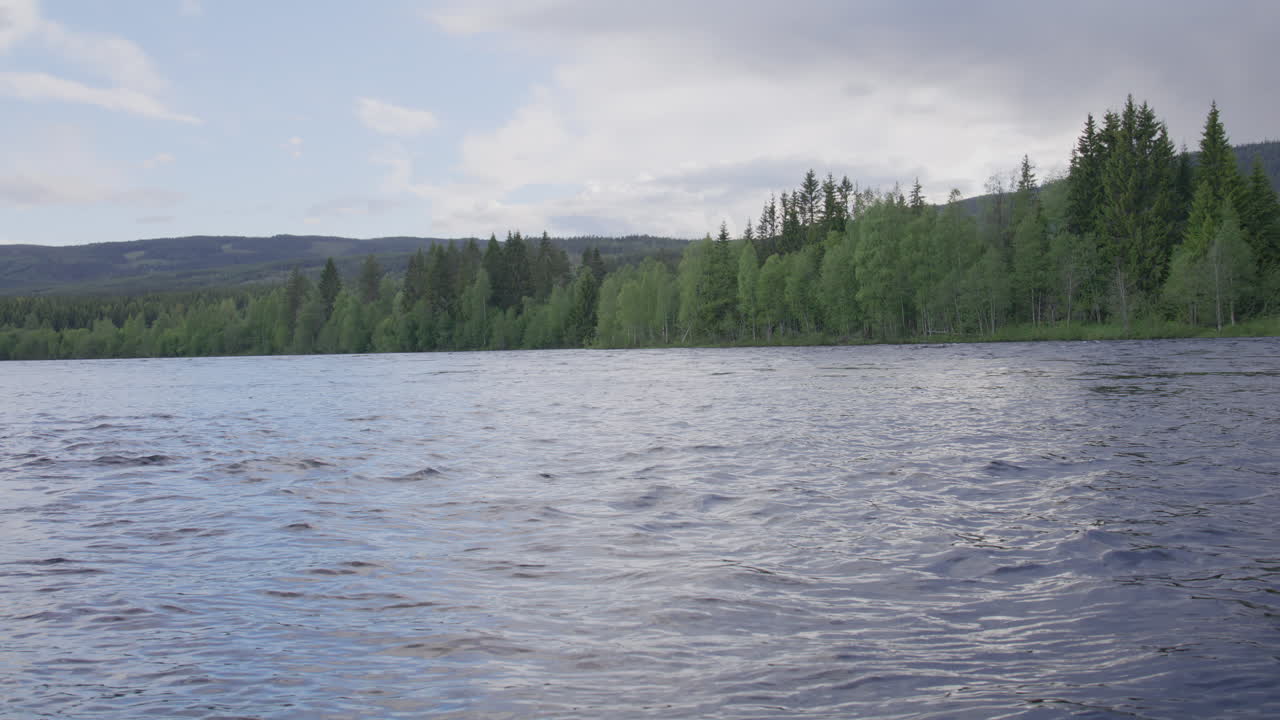 Wide view of Glomma river in Norway with gently rippling water and lush green forest along the shoreline under a lightly clouded sky, showcasing peaceful natural scenery and environmental calmness.