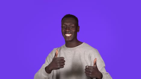 young african american man smiling and dancing in good mood on blue background. unstoppable fun, happiness, thumbs up, human emotions