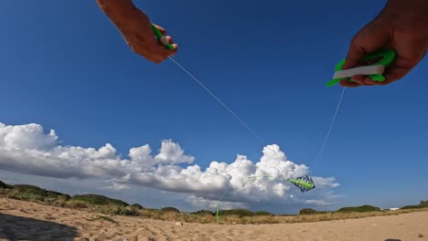 low angle pov of male hands controlling flying green kite over sandy beach by holding green handles