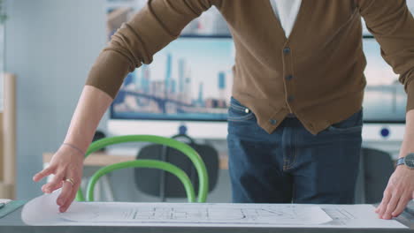 male architect in office unrolling plan or blueprint and laying it on desk before making notes