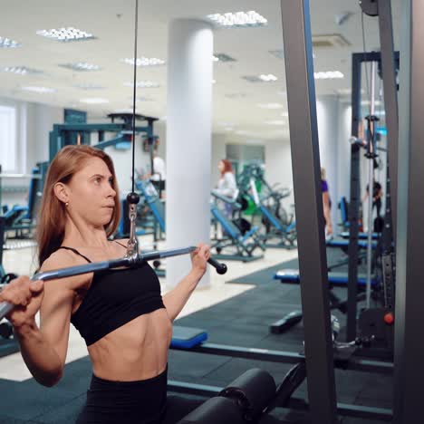 a pretty athlete with loose hair performs an exercise to strengthen the pectoral muscles, surrounded by professional sports equipment in the gym.