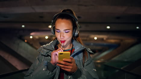 Playful-girl-listening-music-by-earphones-using-internet-app-on-phone-close-up.