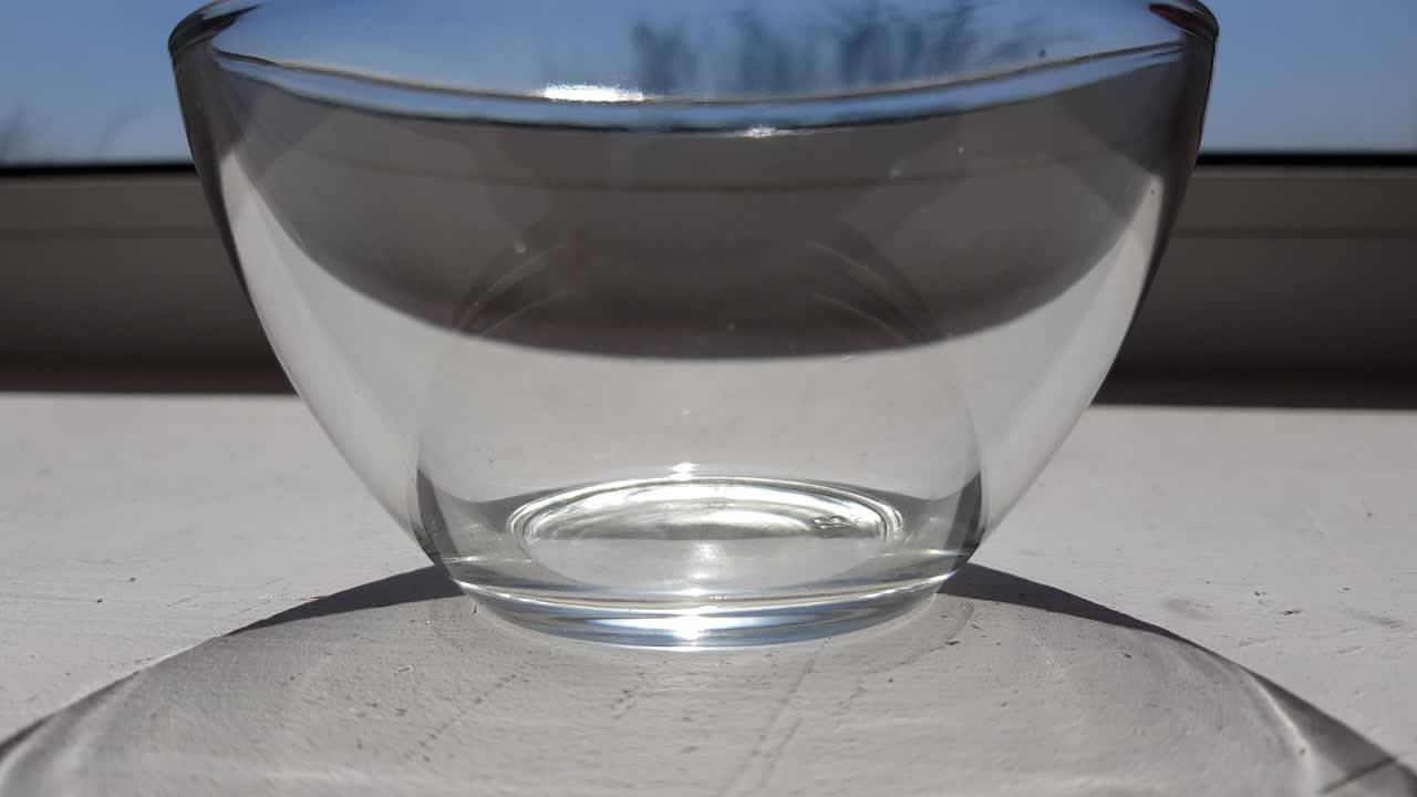 un cuenco de vidrio transparente vacío en un alféizar blanco. fondo azul soleado del cielo