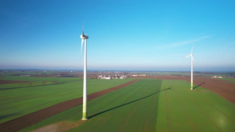 large spinning windmills standing on lush green field in poland on sunny spring day - drone shot side dolly