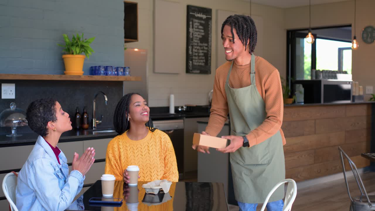 Arranging pastries male barista serving pastry box to diverse female friends at cafe, copy space