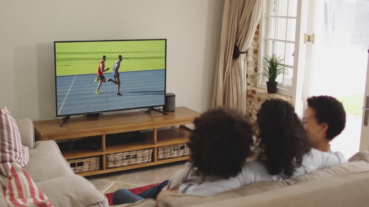 Composizione di famiglia felice seduta insieme a casa che guarda un evento di atletica leggera di corsa in TV.
