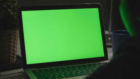 over the shoulder shot of a young boy using on laptop computer on desk, looking at green screen. dolly shot 60fps.