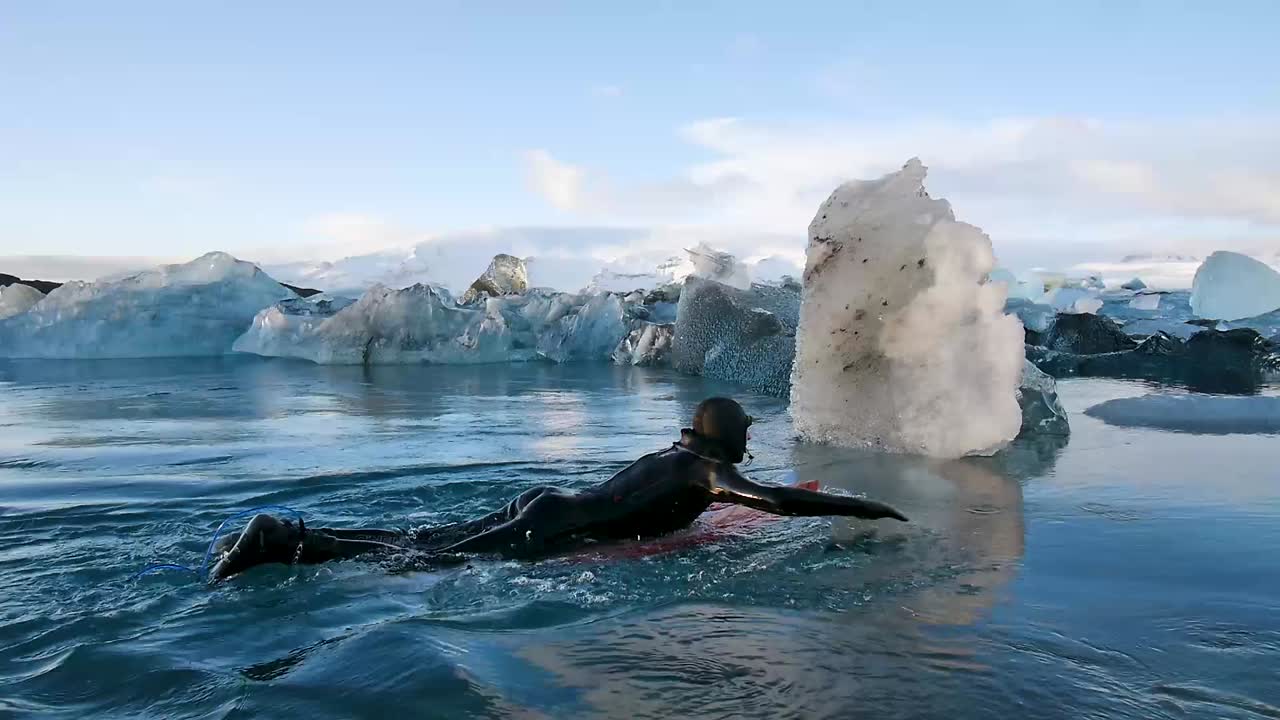 surfista remando a través de icebergs en un río congelado en islandia