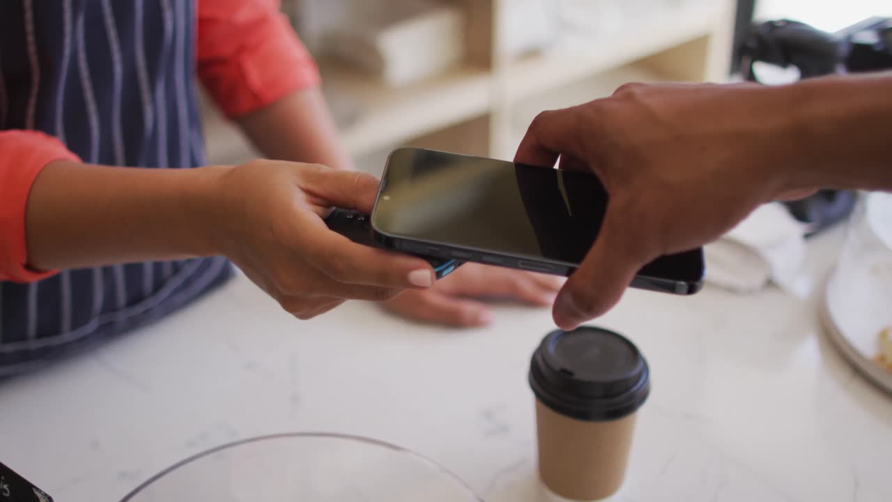 video de las manos de un hombre biracial pagando con un teléfono inteligente por café