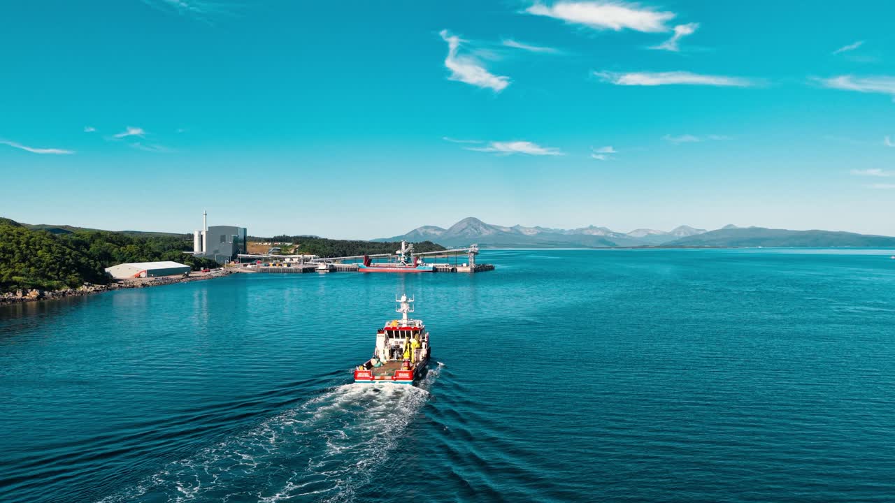 Boat sailing on the sea near industrial port with mountain views