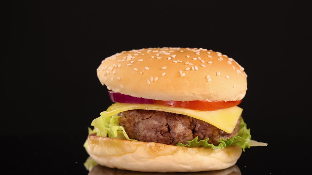 A classic beef burger with lettuce, tomato, onion, and cheese rotates smoothly on a black seamless background under bright studio lighting, highlighting fresh ingredients