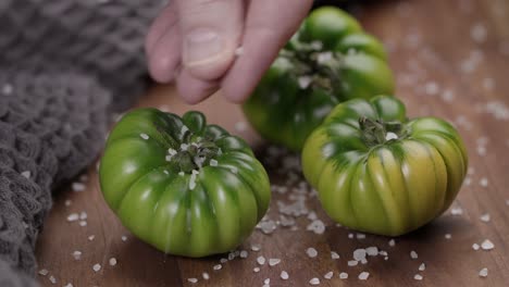 Close-up-shot-of-green-tomatoes-kept-on-a-wooden-surface-with-salt-sprinkle-over-it-for-food-photography