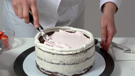 front shot of a baker using an icing spatula to carefully touch up sides of cream covered cake.