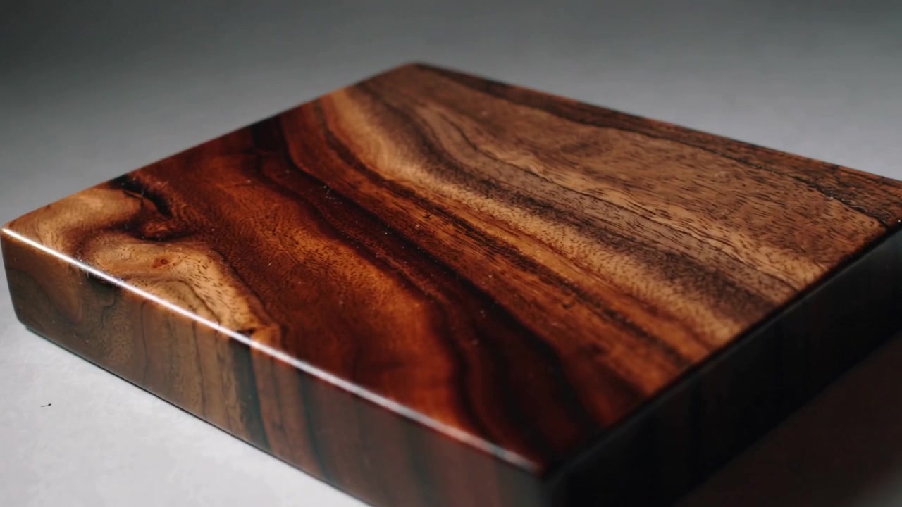Entrando dal bordo superiore, un pennello stende la finitura su un blocco di legno su un tavolo grigio.
