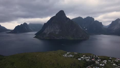 Flying-over-Nordic-village-towards-fjords-and-dark-grey-glassy-water-in-Norway