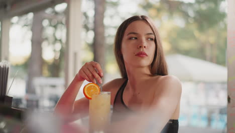 una mujer infeliz agita un cóctel con paja en el bar. una mujer triste piensa en problemas de relación bebiendo alcohol en el bar de la playa. ubicación de verano en un complejo marítimo