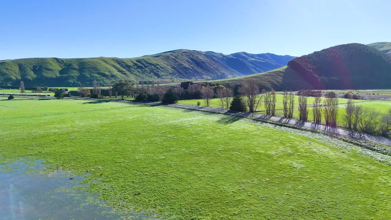 Aerial footage captures Akaroa's vibrant green fields and rolling hills under clear blue skies, showcasing serene natural beauty