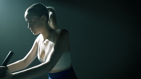 waist-up shot starting from the woman’s back, gliding through her profile to a frontal view as she pedals with intensity. cinematic lighting highlights her motion, sweat, and focused physical effort