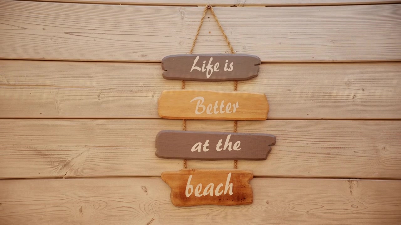 Decorative wooden beach sign reading Life is Better at the Beach mounted on a light wooden wall