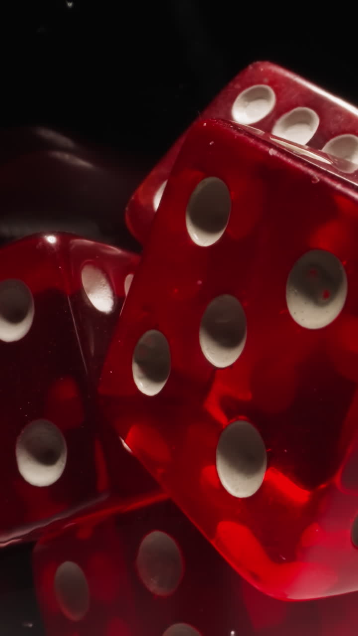 Red dices with white dots thrown into transparent glass illuminated by bright studio light. Gaming cubes with equal points on faces in wineglass on black background macro