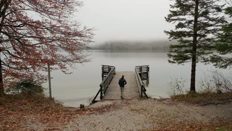 a man walking away from the camera onto a wooden pier on a lake