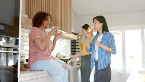 three women friends enjoying drinks and chatting together in modern kitchen