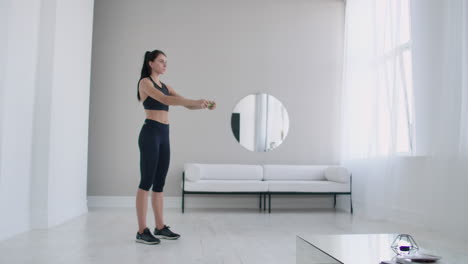 la mujer morena hace calentamiento y ejercicios en su apartamento por la mañana gira el cuerpo a ciegas y a la derecha con los brazos enderezados.