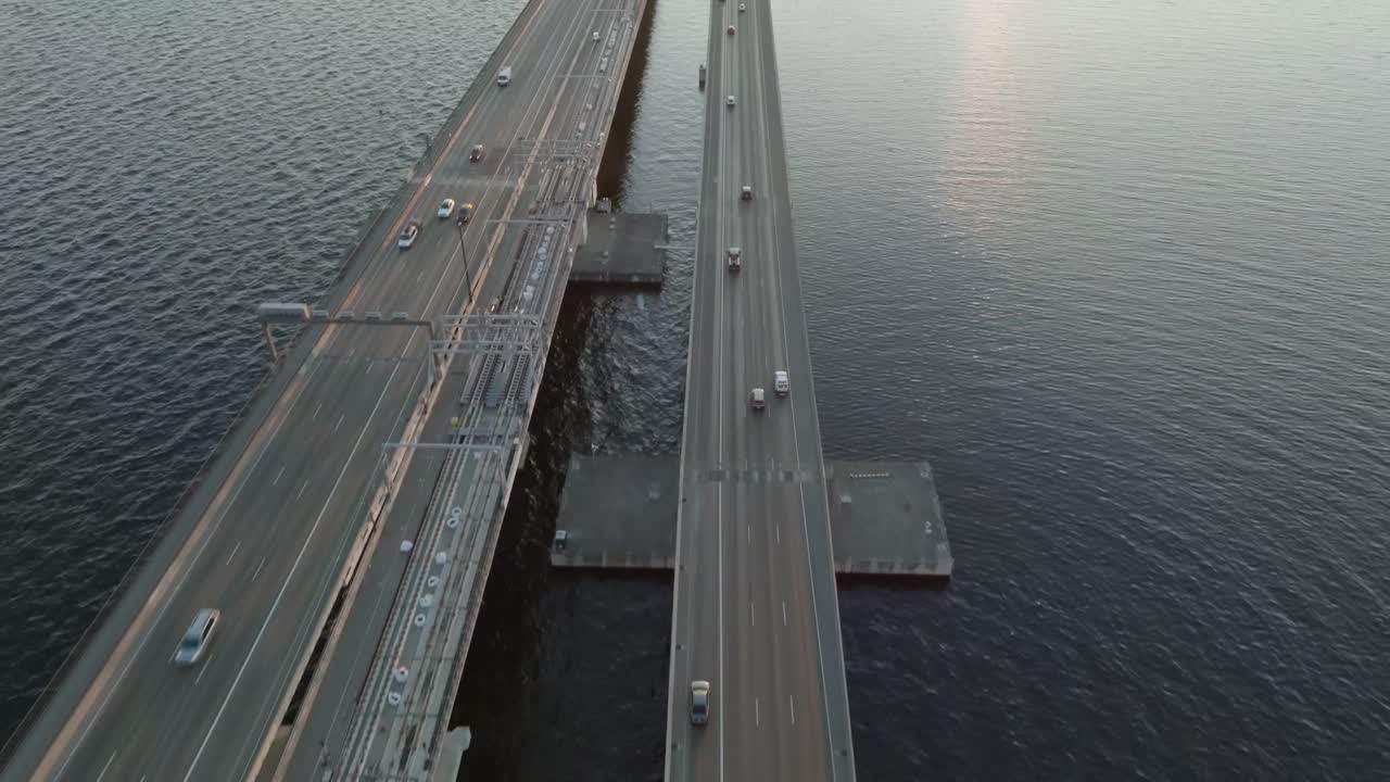 Captivating drone flight during the golden hour showcases a beautiful sunset over Seattle’s stunning floating bridge. The traffic of cars adds a cinematic touch to the scene.