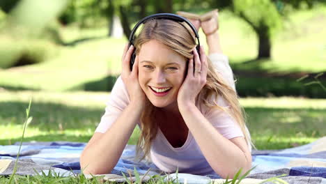 chica feliz acostada en una manta escuchando música en el parque