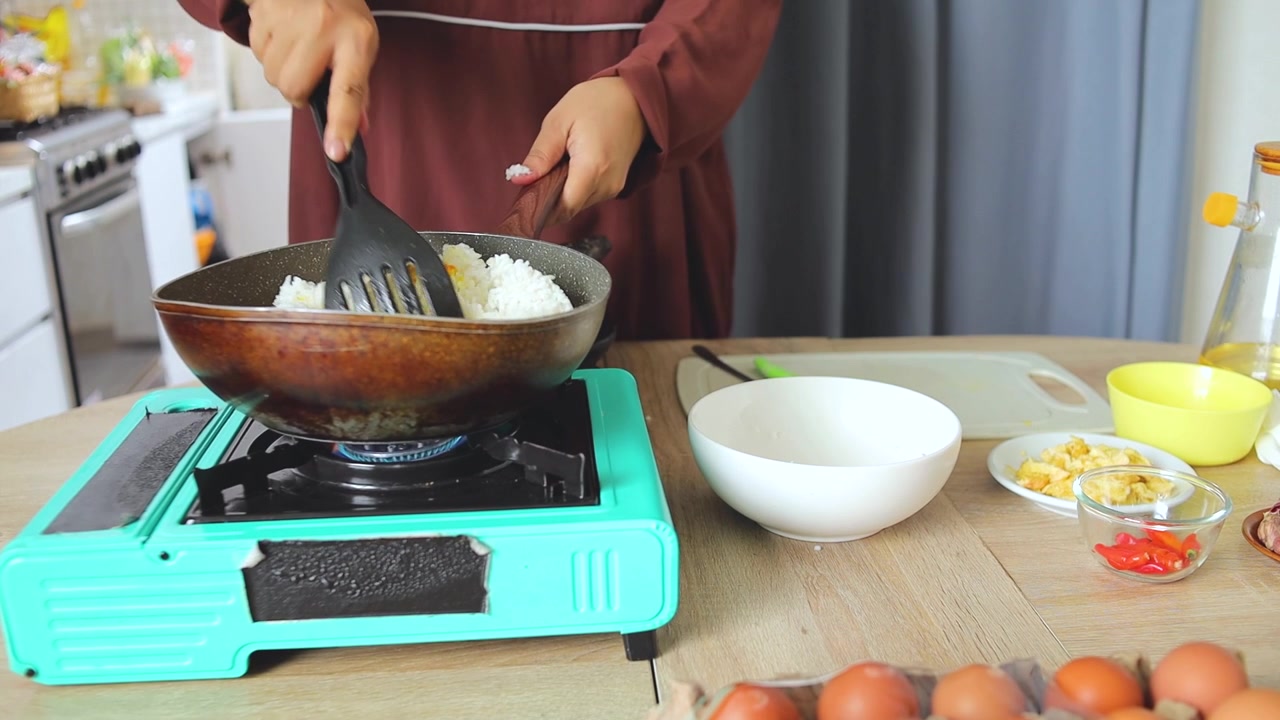 Tangan wanita menuangkan nasi putih ke wajan panas dan mengaduknya dengan spatula untuk memasak nasi goreng.