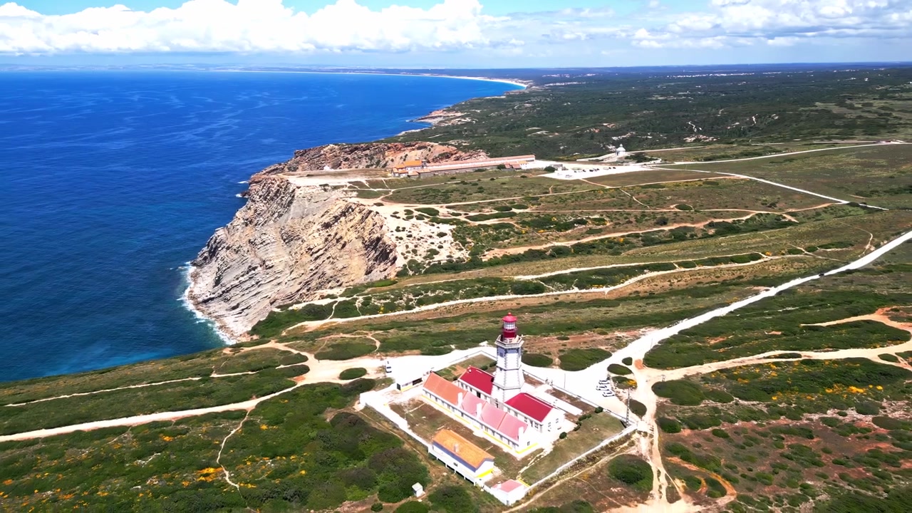 Vista aerea che si avvicina a un faro costiero in cima a scogliere frastagliate e al paesaggio circostante.