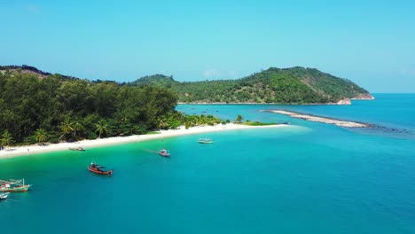Paradise-bay-with-calm-clear-water-of-turquoise-lagoon-and-anchored-boats-near-exotic-beach-under-palm-trees-in-Thailand