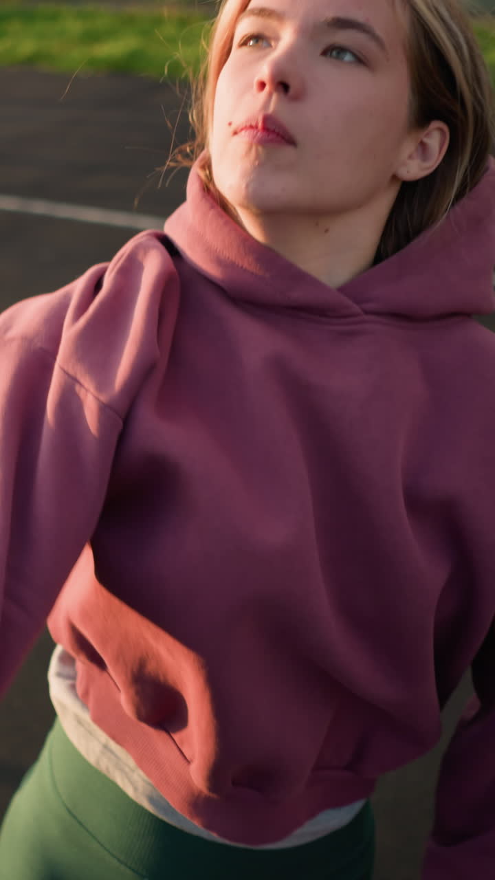joven atleta con capucha marrón saltando voleibol, preparándose para servir en una cancha al aire libre con vegetación en el fondo y claras marcas de cancha visibles en el suelo