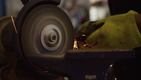 Front-side-view-of-metal-being-shaped-by-bench-grinder,-igniting-sparks-4K-slow-motion