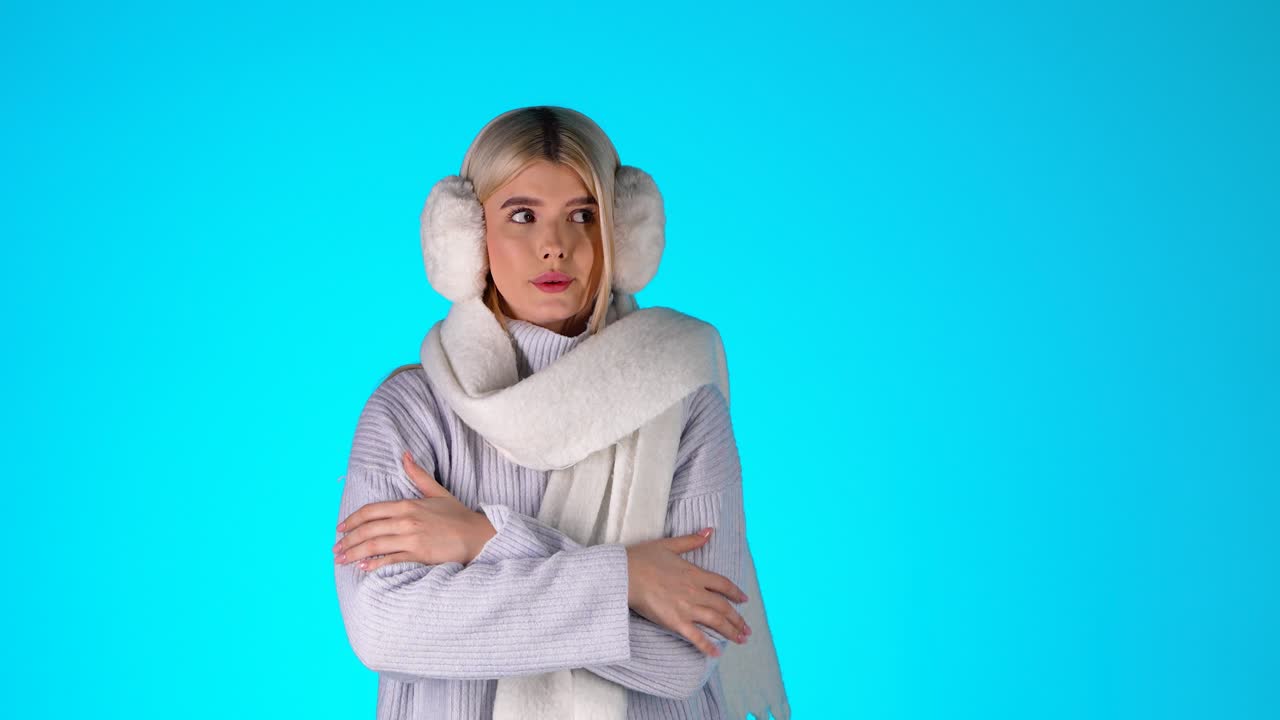 젊은 금발 여성의 초상화, 차가운 느낌, 스카프 스웨터와 귀막을 입고, 파란색 배경으로 스튜디오 촬영