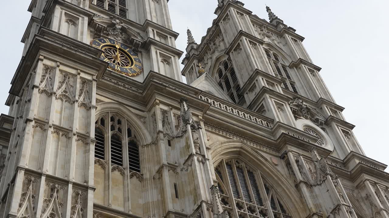 Abbazia di Westminster a Londra, che mostra le torri gemelle e l'orologio sulla facciata da un'angolazione bassa. Vista diurna con dettagli architettonici gotici.