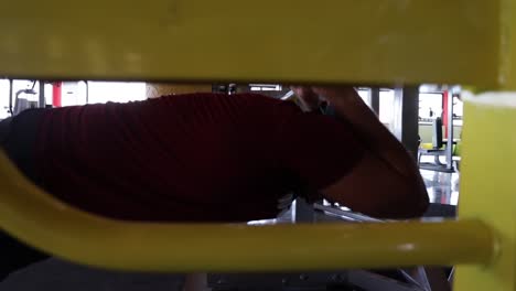 joven caucásico con sombrero al revés hace ejercicio de tríceps con barra estacionaria en el gimnasio, perfil de cierre