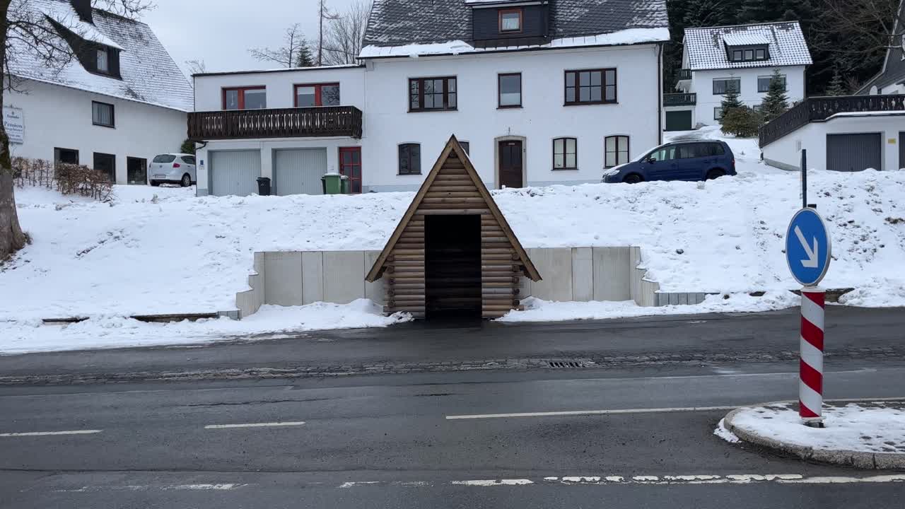 pequeña casa de madera en una carretera con coches pasando por la nieve en invierno con edificios de apartamentos en el fondo