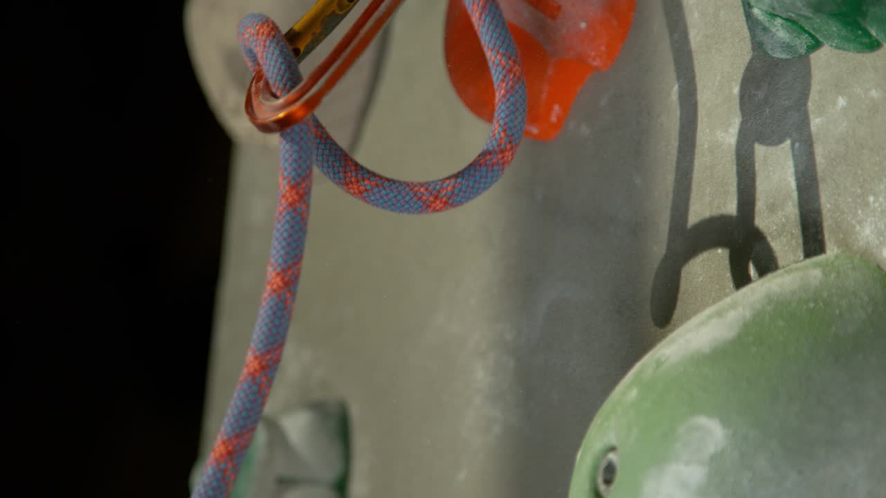 macro: una cuerda de fijación de colores se desliza de un carabiner y cae a lo largo de la pared