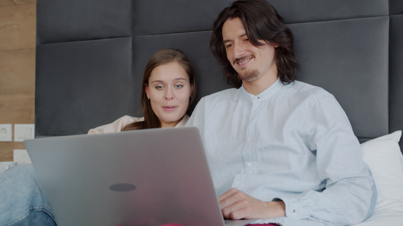 una pareja viendo una computadora portátil en la cama.