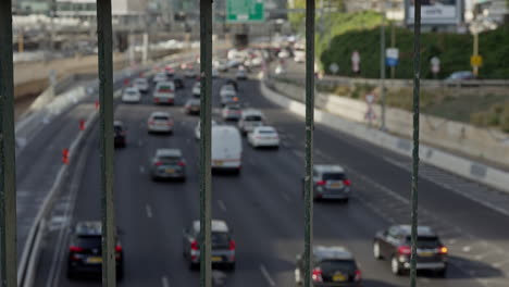 traffic driving away from camera at hashalom azrieli in tel aviv israel through bars on bridge overlooking road. wide shot static. bars in sharp focus, traffic slightly defocused. 50fps