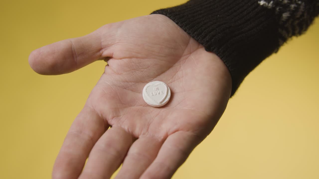 노란색 배경에 사랑의 메시지와 함께 심장 사탕을 들고 손을 가까이