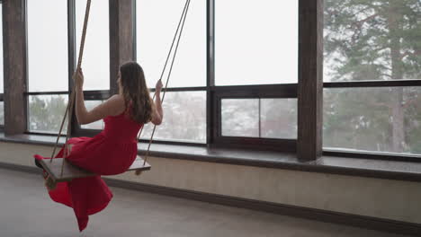 mujer de vestido rojo sentada en un columpio junto a una ventana