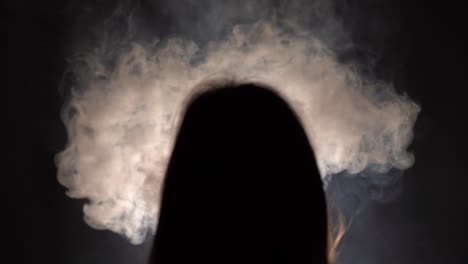 isolated slow motion silhouetted closeup of a person with long hair binge smoking in a dark room facing a dark wall