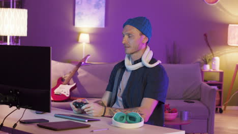 man sitting at desk and holding a snake around his neck while playing video games on the computer