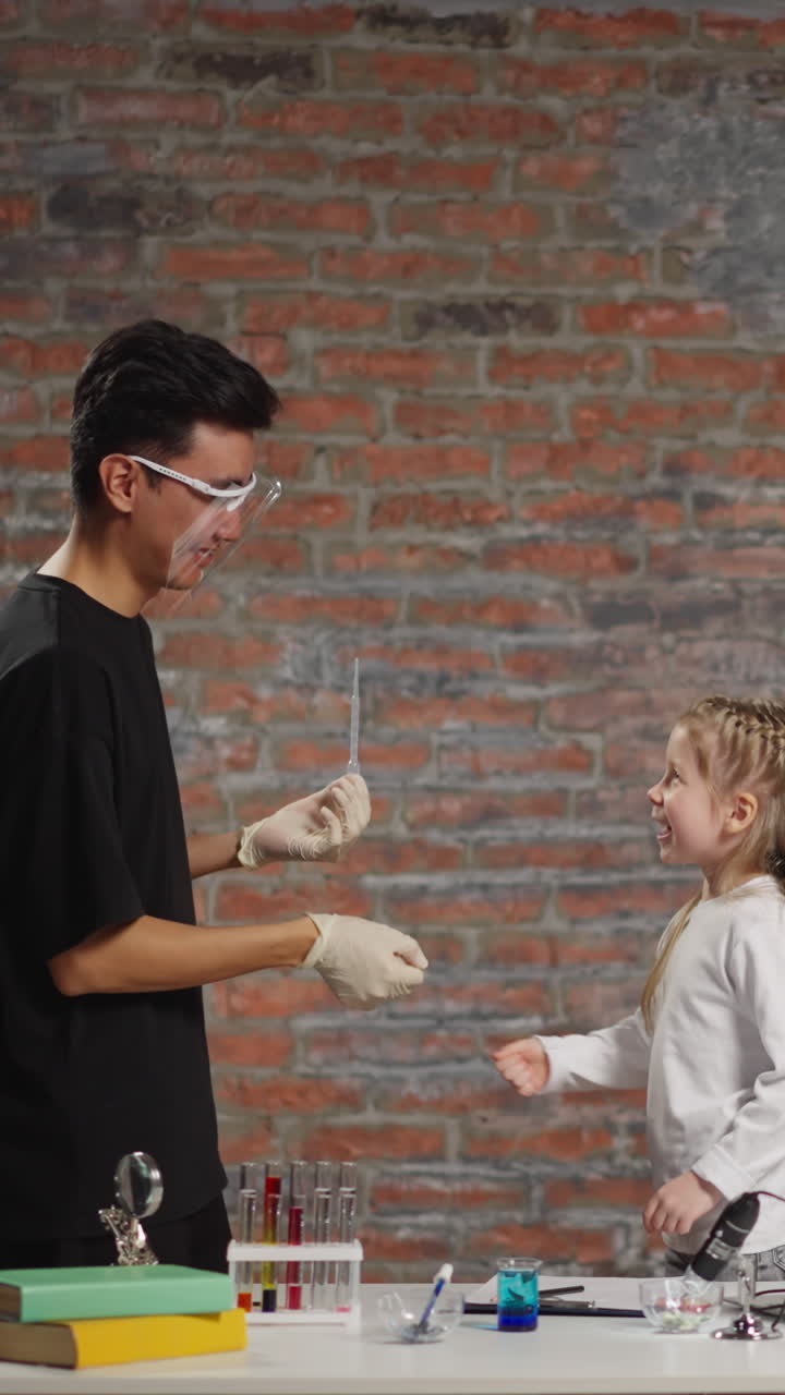 Asian chemistry tutor and pretty preschooler girl play rock paper scissors choosing next experiment at fun science lesson in spacious classroom