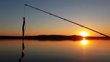 a bass fishing lure dangling from a fishing rod with a perfect sunset over a calm lake in the background