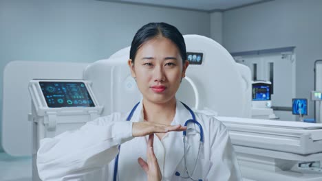 Close Up Of Asian Woman Doctor With Stethoscope Doing Time Out Gesture With Hands With Mri Machine In The Hospital