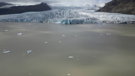 Vista-Aérea-Desde-La-Laguna-Llena-De-Icebergs-De-Fjallsárlón,-Con-Increíbles-Formaciones-De-Hielo,-Colores-Blanco-Y-Azul-Con-Una-Hermosa-Vista-De-La-Laguna-Donde-El-Hielo-Flota-En-Islandia-Durante-El-Verano