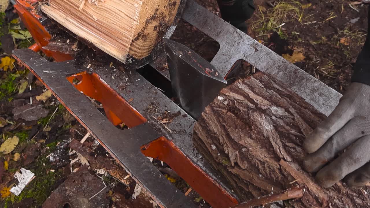 Top down view of a pine firewood log timber being split in half by a wood splitter machine in slow motion in autumn nature during day time, with wood chips and fallen leaves on the bokeh background